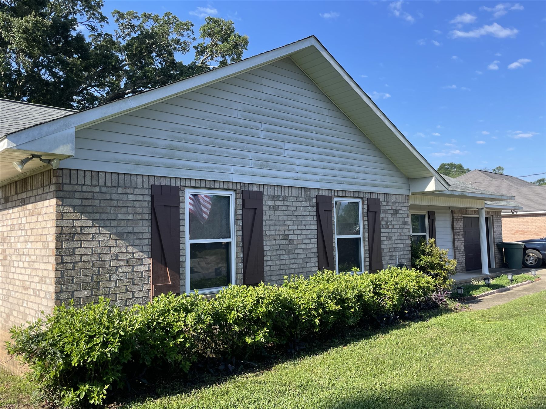 Gray-green mildew streaking on the gable siding and brick of a house, before washing