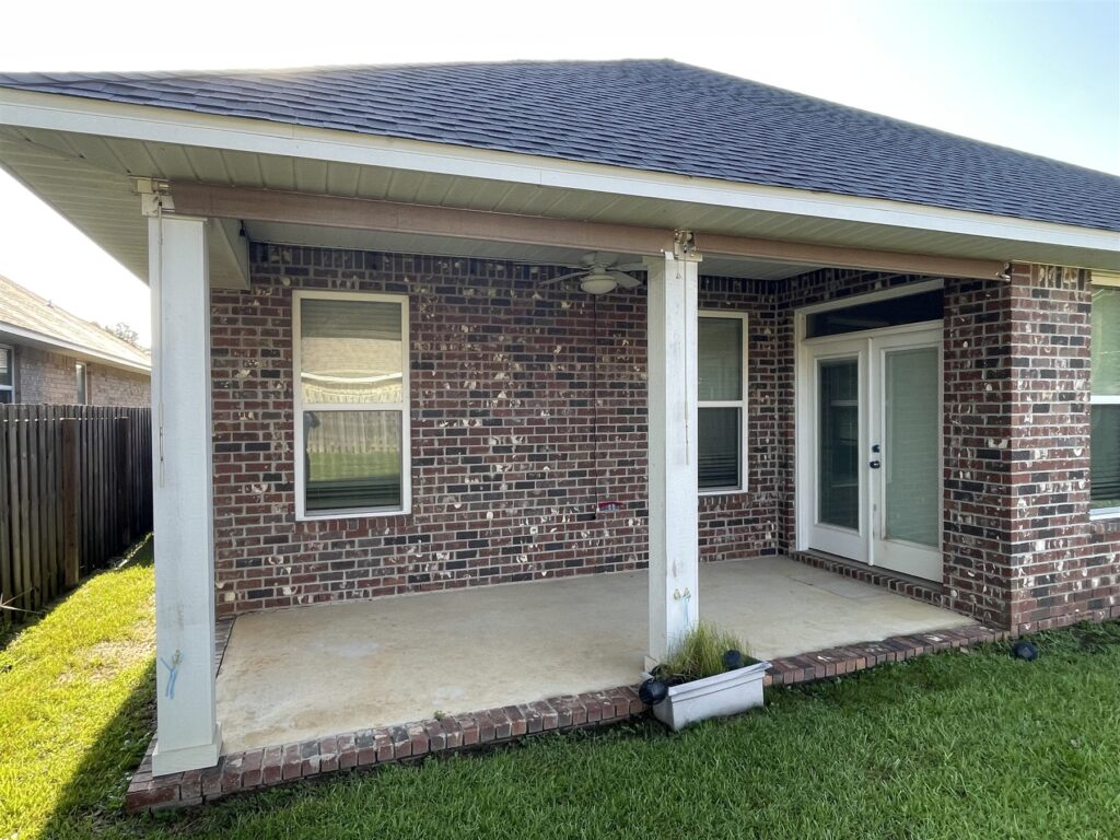 A brick covered back patio with white columns and a clean concrete floor