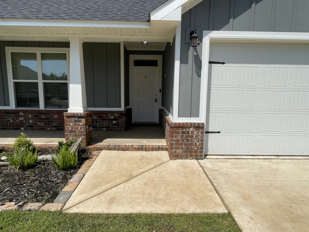 A front entry with a white door, brick porch base and clean concrete walkway beside a garage